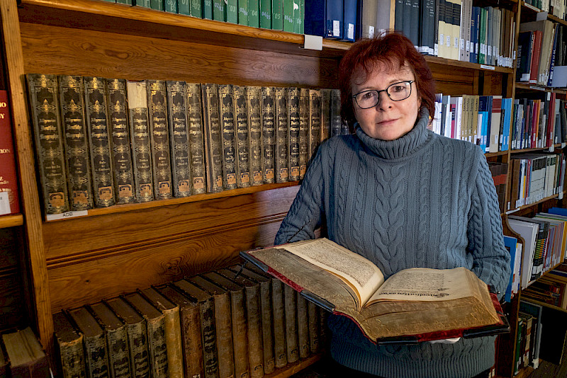 Karin Keller hält im Forschungssaal des Universitätsarchivs das 1632 angelegte Wittenberger Statutenbuch in der Hand, in das unter anderem ein Horoskop zum Gründungstag der Universität Wittenberg eingebunden ist.