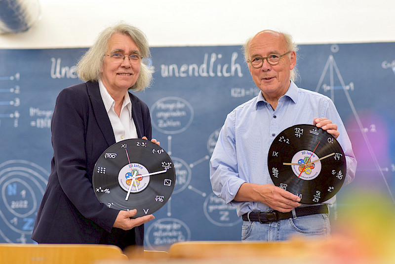 Werkstatt-Leiterin Karin Richter und Wilfried Herget, ein früher Begleiter des Projekts. In der Hand halten sie besondere Geschenke zum Jubiläum: Mathematik-Uhren.