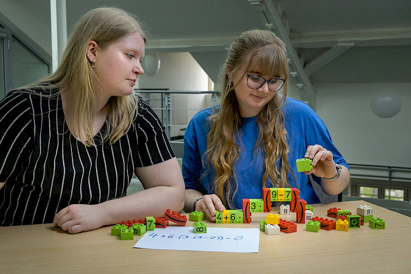 Student teachers Sarah Schmohl (left) and Paulina Wieland try out the “bracket mountain” technique, which can be used to visually structure  calculation steps. The calculation is done from “top to bottom”.
