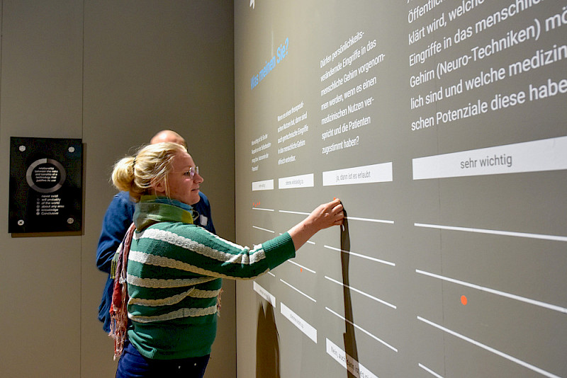 An einer Wand wird können die Besucherinnen und Besucher mit roten Klebepunkten ihre Meinung zur Optogenetik hinterlassen.